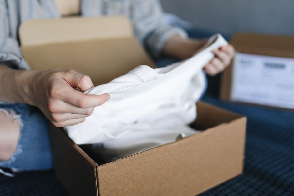 Close-up of a person unboxing a clothing item in a cardboard package indoors.