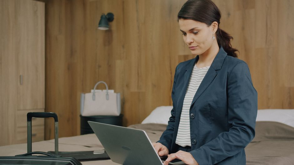 Professional woman using a laptop in a hotel room, preparing for business travel.