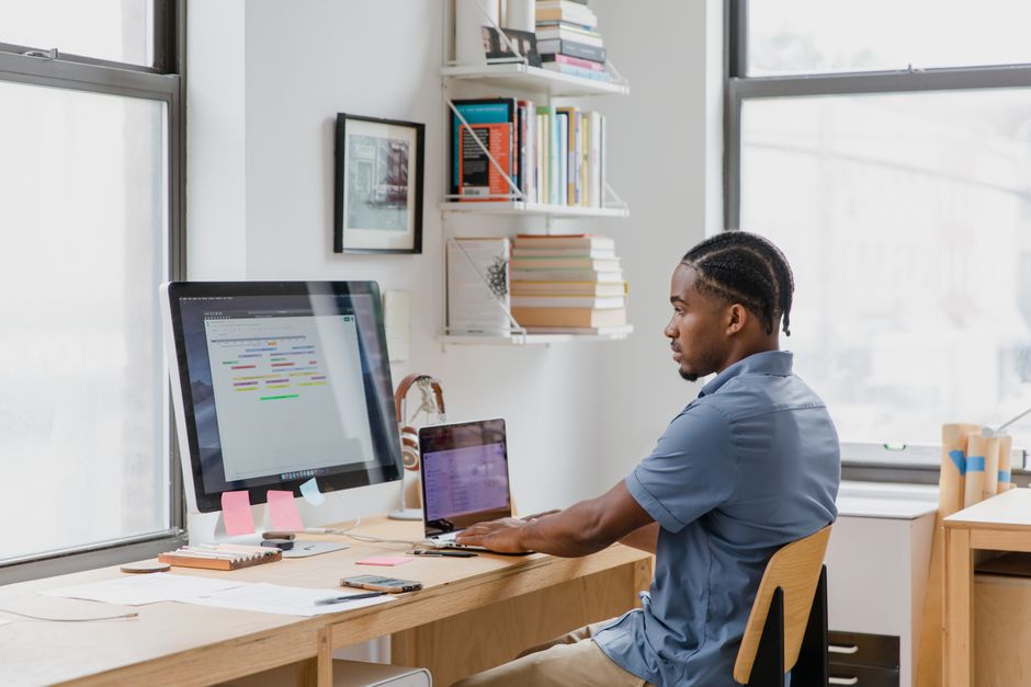 Focused man at home office desk working on dual screens.